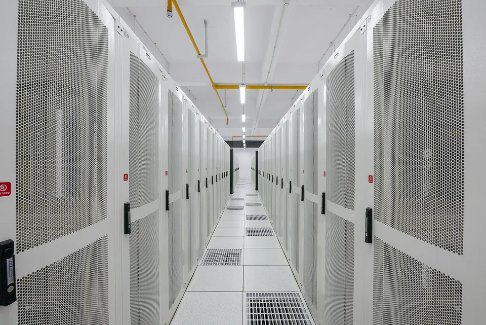 A data center aisle between rows of enclosed server cabinets above a raised floor.